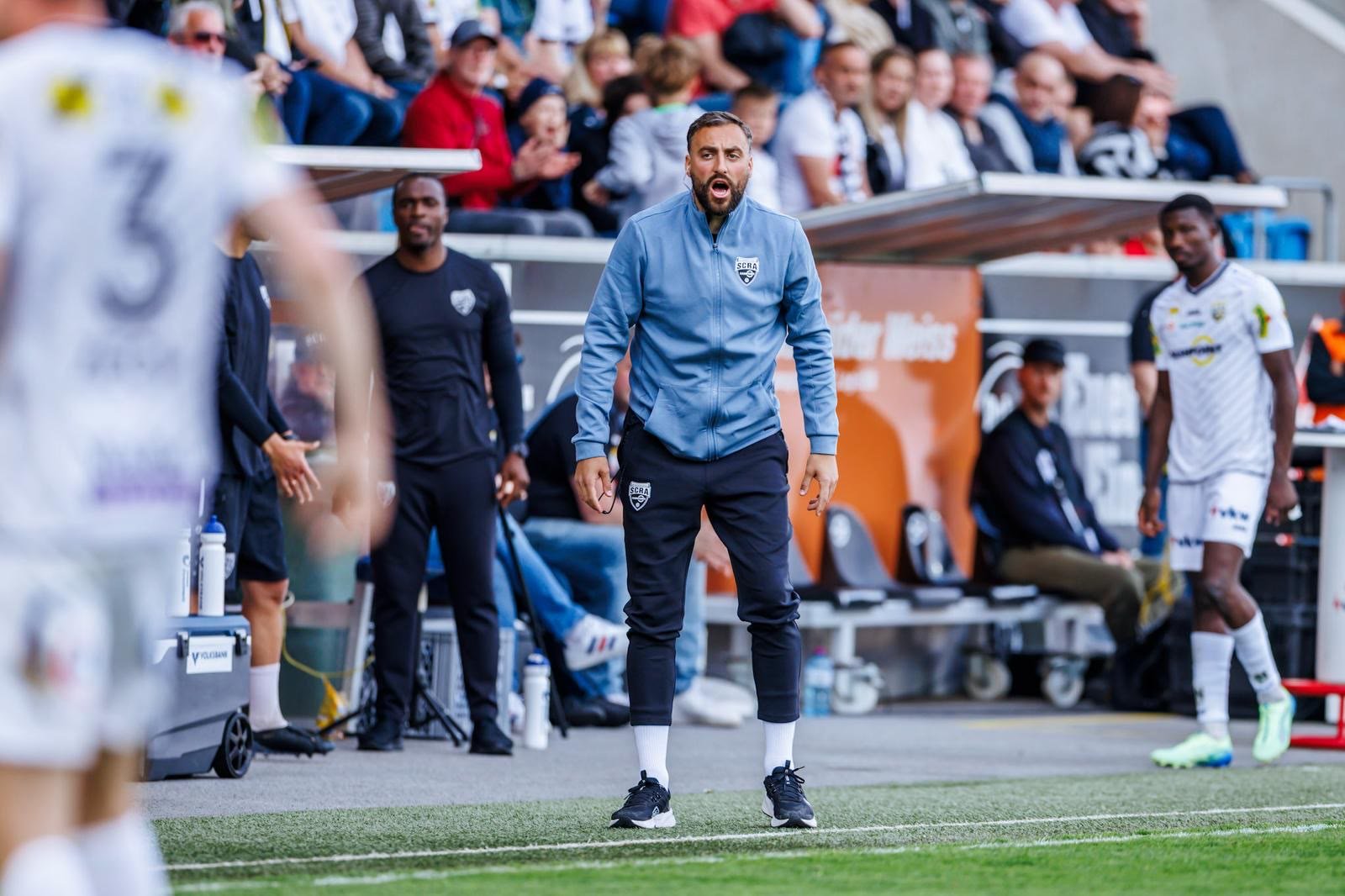 Atdhe Nuhiu als Co-Trainer in hellblauer Trainingsjacke am Spielfeldrand